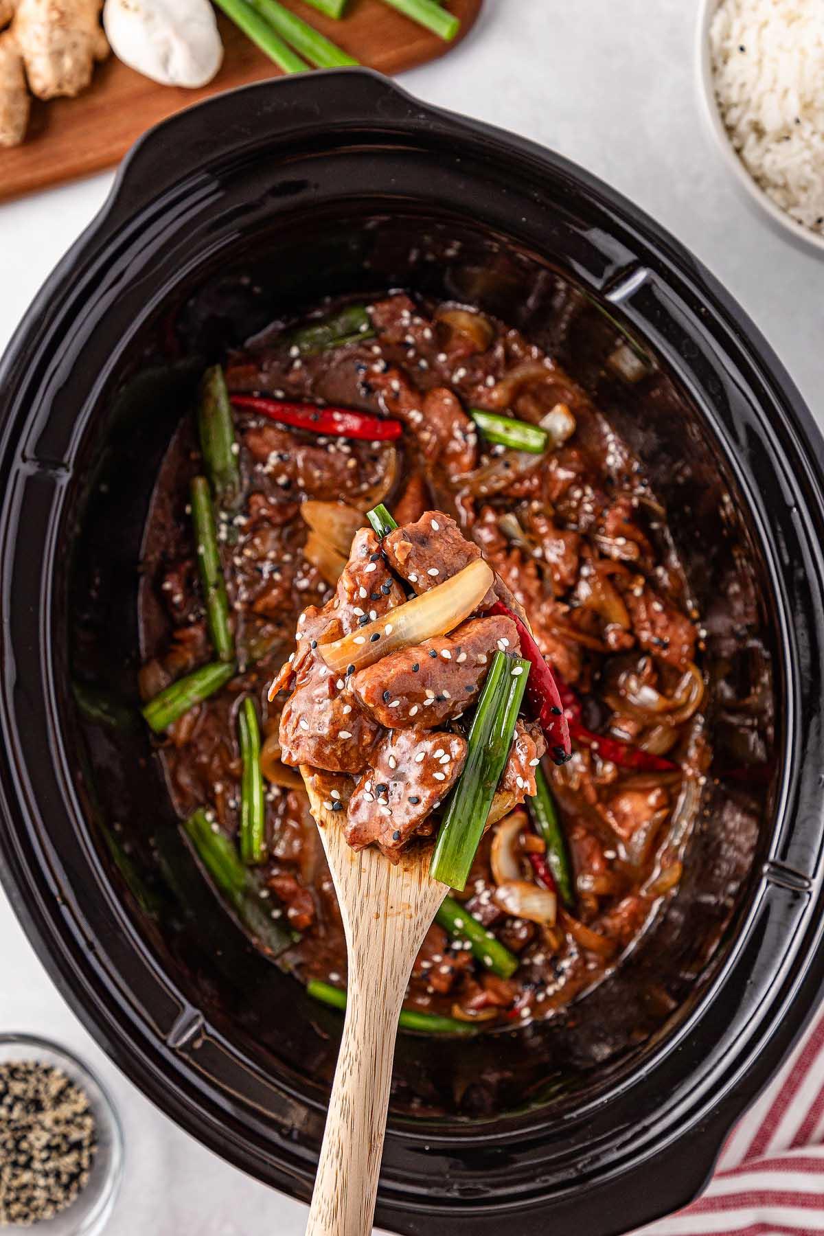 **Σιγομαγειρεμένο Μογγολικό Βοδινό** 11 Slow cooker Mongolian beef stir-fry with sliced beef, fresh vegetables, and sesame seeds, being served with a wooden spoon.
