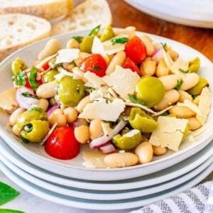 Ιταλική Σαλάτα Λευκών Φασολιών 12 Μια πιατέλα με ιταλική σαλάτα λευκών φασολιών με ντοματίνια, ελιές, ξύσματα τυριού και μυρωδικά, περιτριγυρισμένη από ένα μπολ με ντοματίνια, φέτες ψωμιού και ένα γυάλινο δοχείο με ελαιόλαδο.