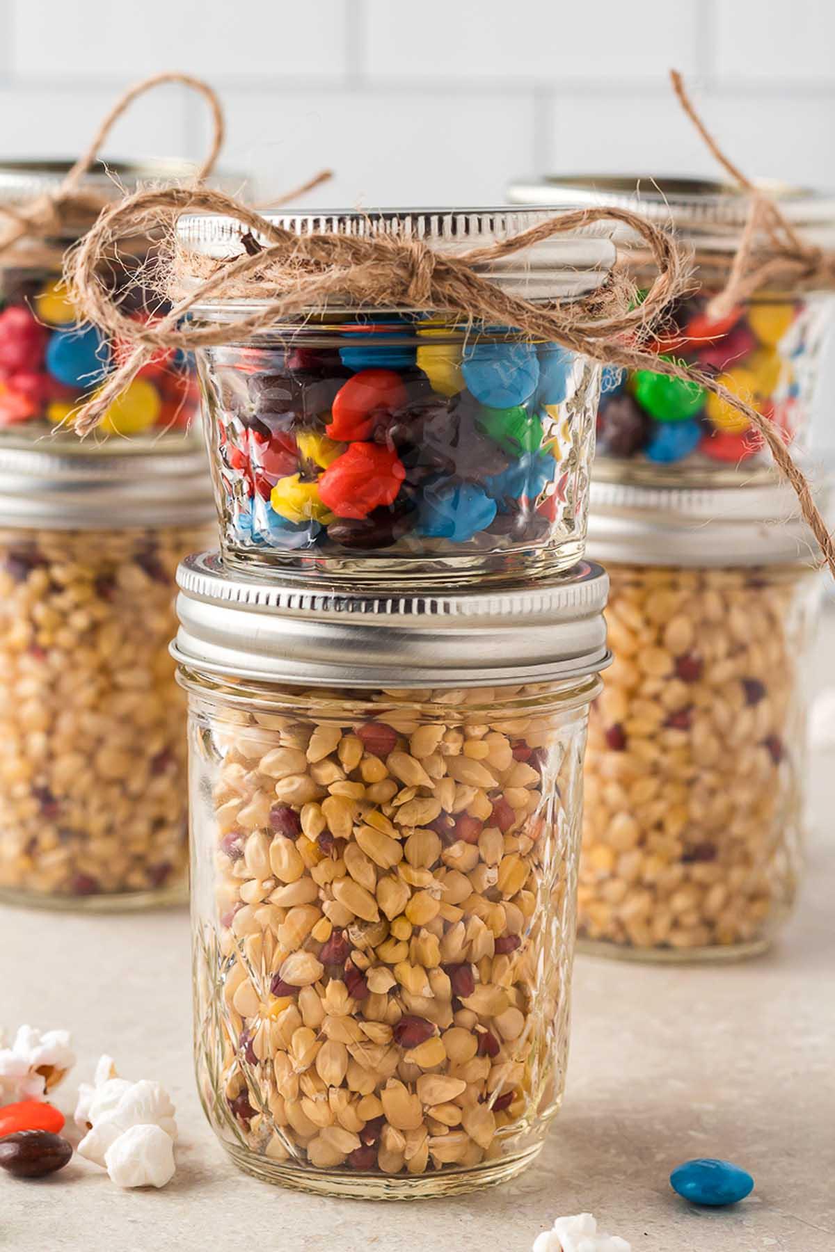 Ποπ κορν με M&M και Σοκολάτα – Σετ Δώρου DIY 14 Τρία γυάλινα βάζα γεμάτα με ξηρούς καρπούς και καραμέλες, μεταμορφωμένα σε ένα απολαυστικό DIY δώρο σε βάζο.