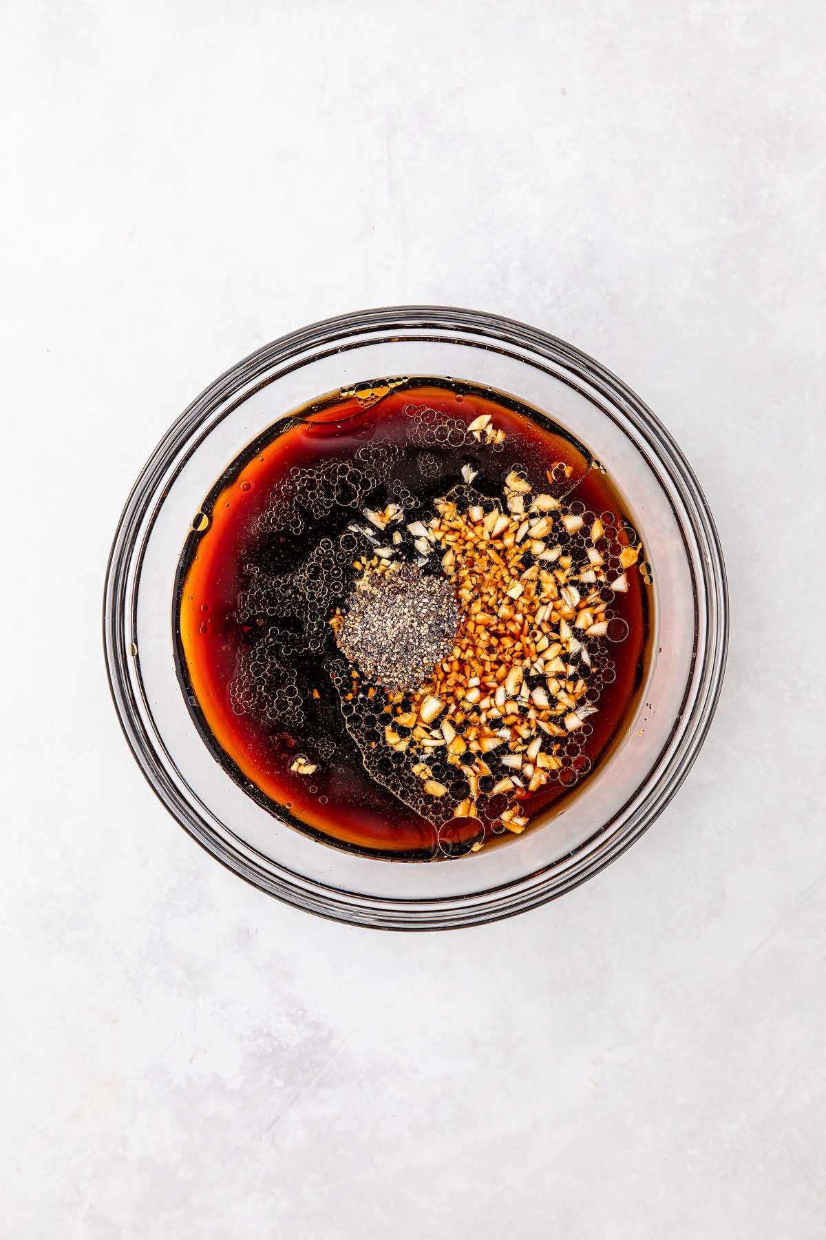 **Σιγομαγειρεμένο Μογγολικό Βοδινό** 15 A bowl featuring a dark, savory liquid reminiscent of slow cooker Mongolian beef, with chopped nuts adding texture and a small mound of ground black pepper crowning the dish.