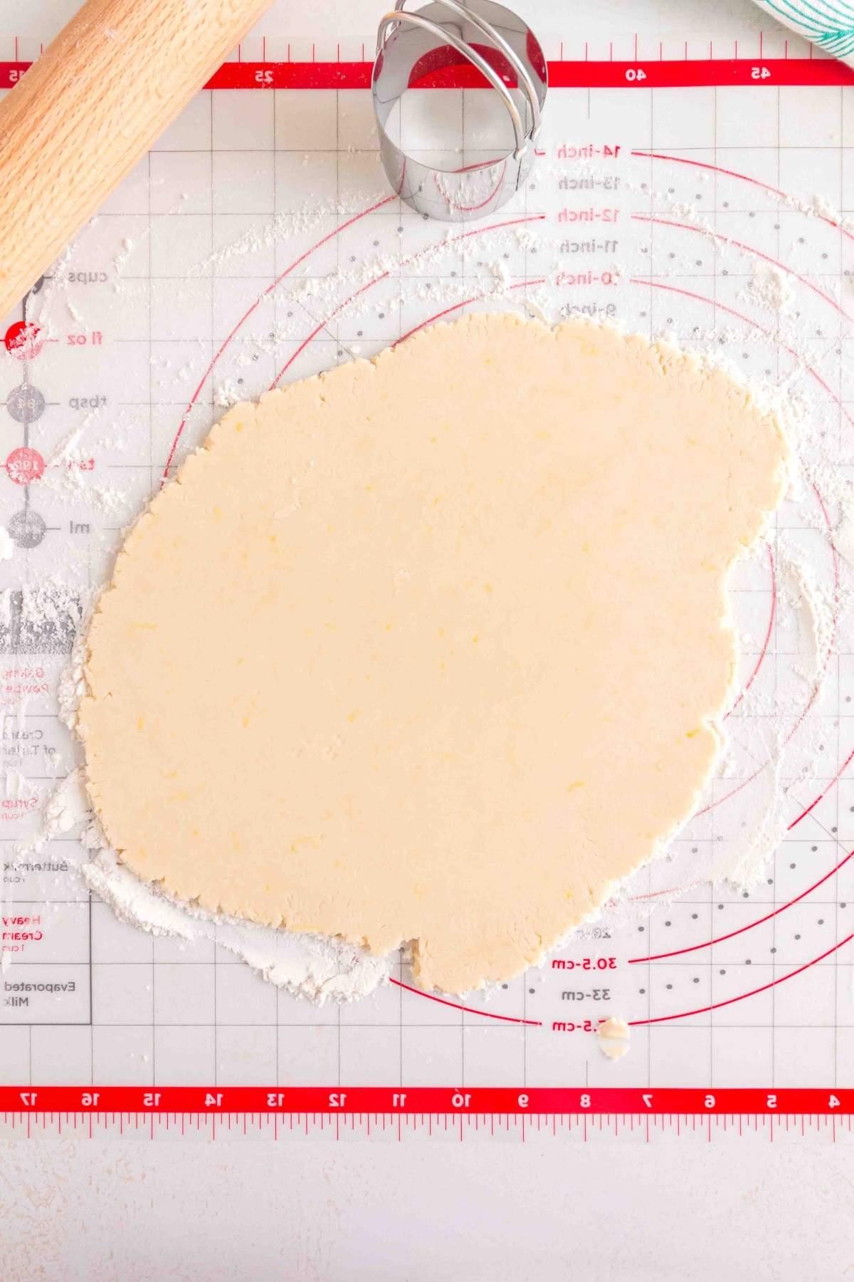 Ανοιγμένη ζύμη για λεμονάτα μπισκότα shortbread σε στρωμένο ταψί ψησίματος, με πλάστη και στρογγυλό κουπάτ κοντά.