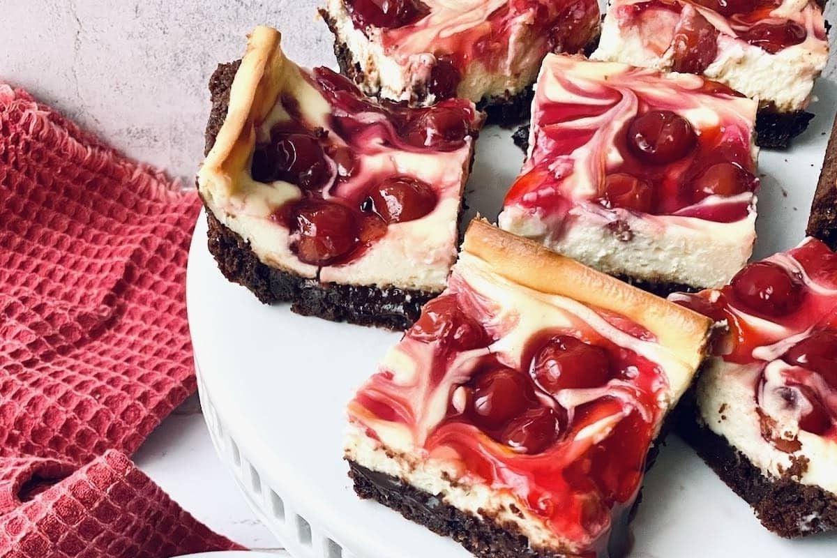 Τετράγωνα σοκολατένιου cheesecake κερασιού σε πιάτο, ιδανικά για όσους αναζητούν νόστιμες συνταγές μπράουνις.