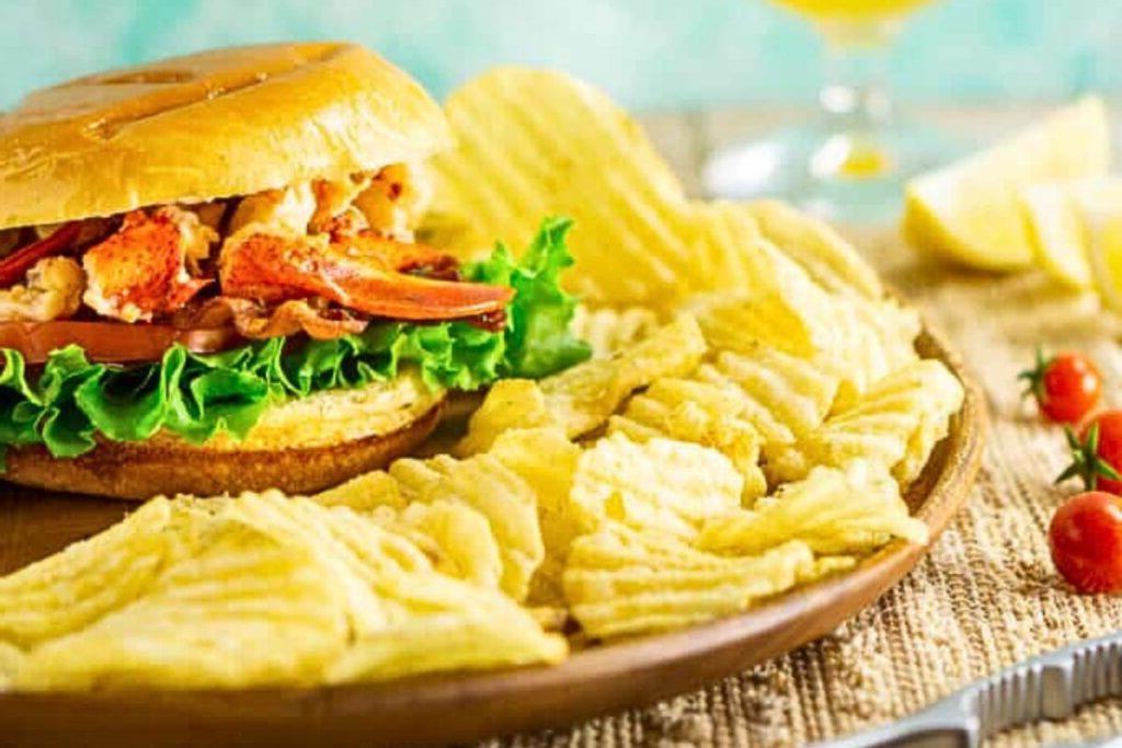 Ένα σάντουιτς BLT αστακού σε ψωμάκι με πατατάκια στο πλάι.