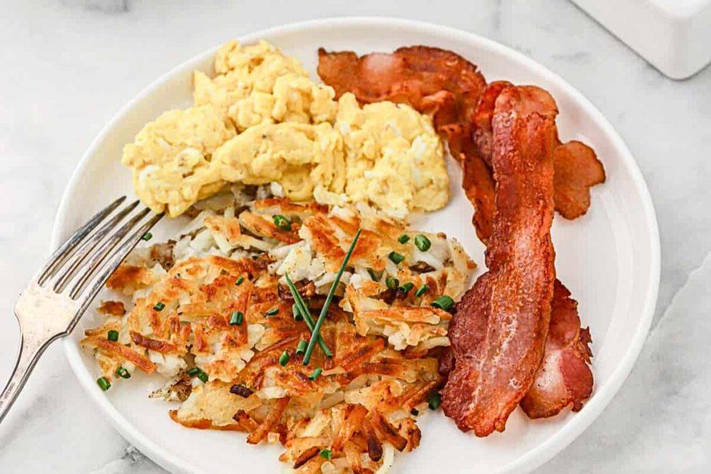 Ένα πιάτο με αυγά, μπέικον και χρυσαφένιες hash browns.