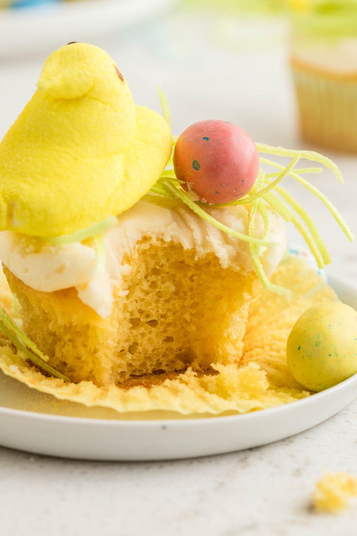 Πασχαλινά Κάπκεϊκς Πουλάκια 6 Cupcake με κίτρινο γλάσο, στολισμένο με ένα κίτρινο ζαχαρωτό σε σχήμα κοτόπουλου και πολύχρωμα ζαχαρωτά αυγά σε πράσινες κλωστές. Ένα μεγάλο κομμάτι λείπει από το cupcake.