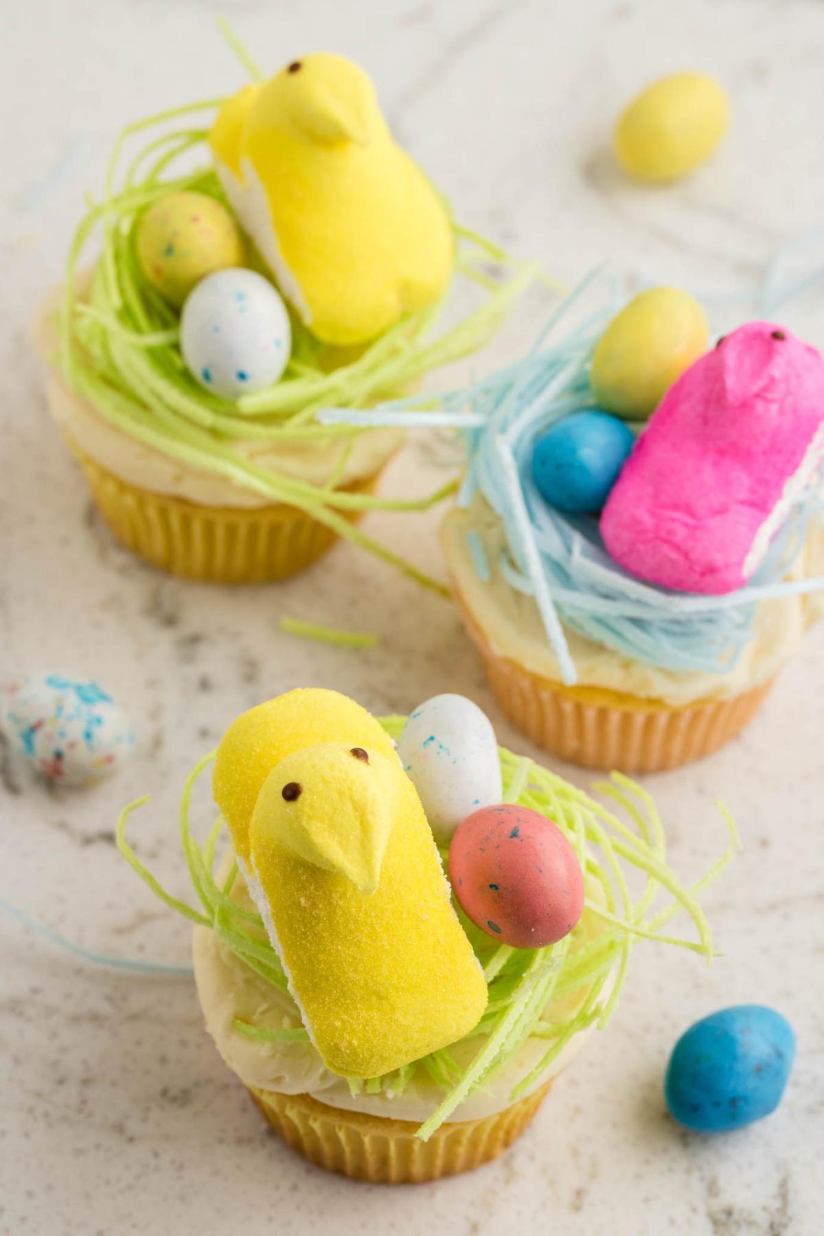 Πασχαλινά Κάπκεϊκς Πουλάκια 7 Cupcakes διακοσμημένα με πράσινο και μπλε γλάσο, στολισμένα με πολύχρωμα μαρσμέλοου κοτόπουλα και στικτά αυγά σε μαρμάρινη επιφάνεια.