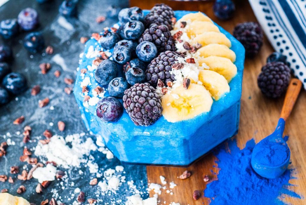 27 Εύκολες Συνταγές Smoothie για να Κάνουν την Ημέρα σας Καλύτερη 8 Ένα μπλε smoothie σε μπολ με φρέσκα φρούτα από πάνω.