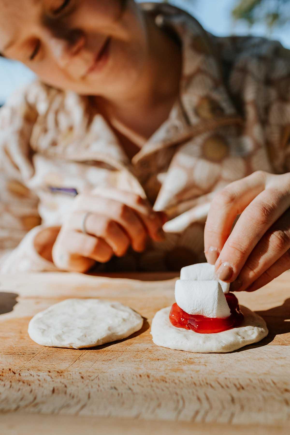 Κερασόπιτα Σίδερου Πίτας 8 Άτομο τοποθετεί marshmallows και γέμιση κερασιών σε ένα κομμάτι ζύμης σε ξύλινη επιφάνεια, ετοιμάζοντας ένα κερασόπιτα βουνού.