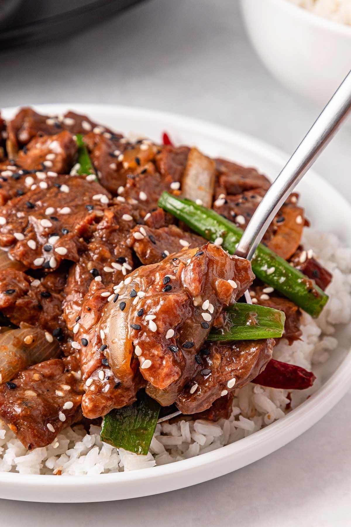 **Σιγομαγειρεμένο Μογγολικό Βοδινό** 9 A plate of stir-fry featuring tender slow cooker Mongolian beef, green peppers, onions, and red chili peppers on rice, garnished with black and white sesame seeds.