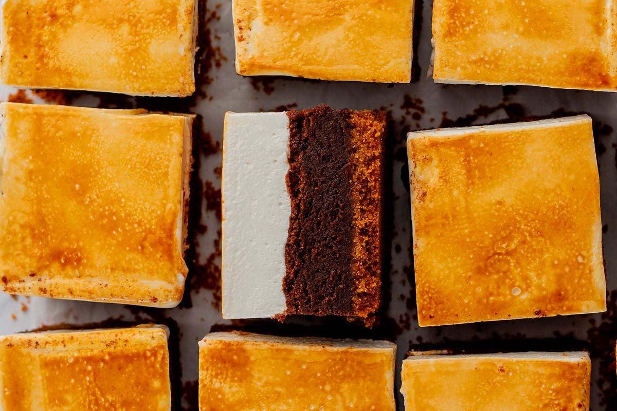 Κοντινό πλάνο S'mores Brownies διατεταγμένα σε ένα πλέγμα. Κάθε τετράγωνο διαθέτει μια στρώση ψημένου marshmallow πάνω από μια βάση σοκολατένιου μπράουνι. Ένα κομμάτι είναι γυρισμένο για να δείξει τις στρώσεις.