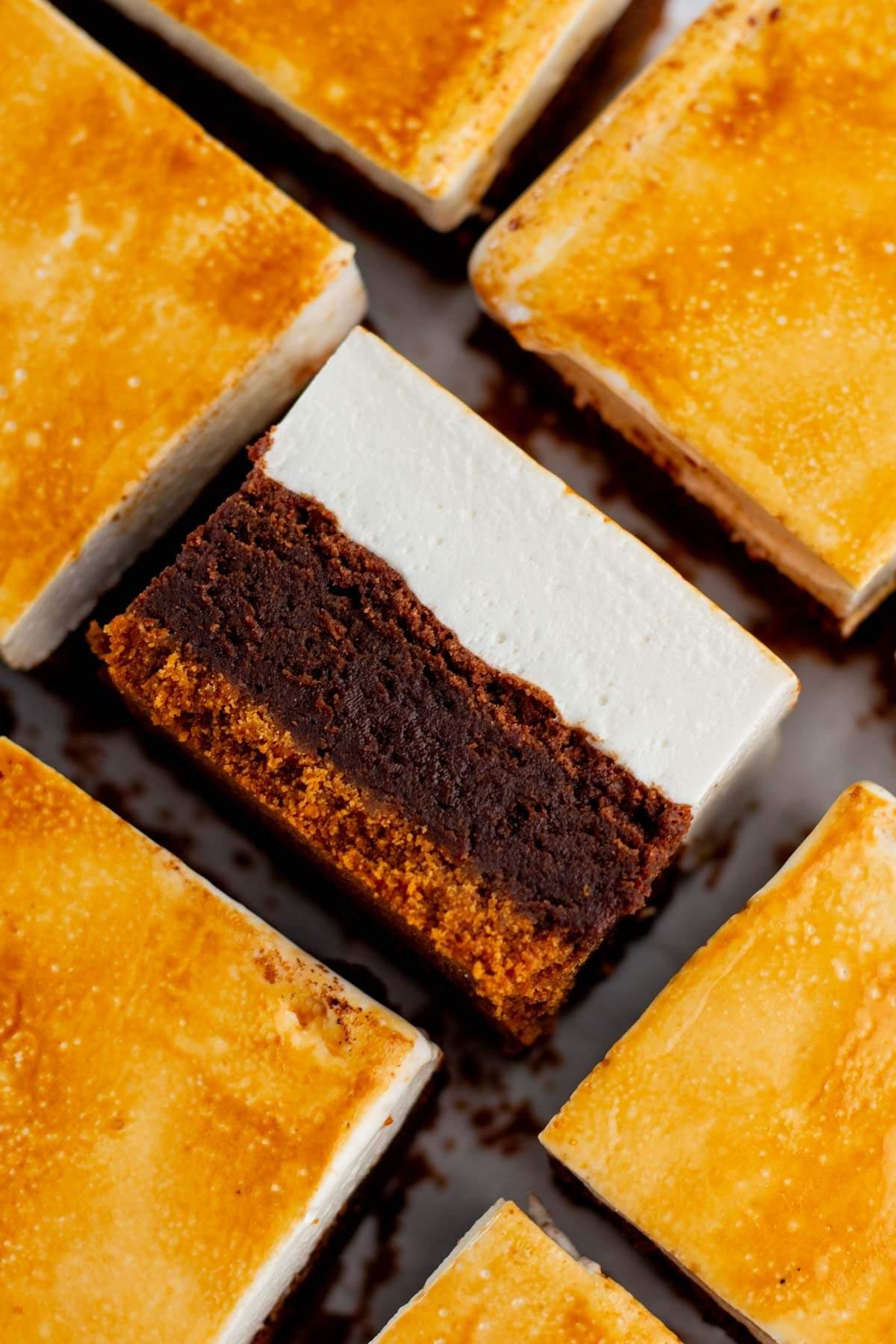 Κοντινό πλάνο τετράγωνων s'mores brownies, το καθένα με πολυεπίπεδη σύνθεση που περιλαμβάνει βάση μπισκότου graham cracker, σοκολατένια μέση στρώση και επάνω στρώση marshmallow. Οι κορυφές είναι ομοιόμορφα ψημένες.