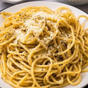 Τυρί και Πιπέρι 12 Ένα πιάτο cacio e pepe, με σπαγγέτι γαρνιρισμένα με τριμμένο τυρί και μια πρέζα μαύρο πιπέρι, είναι όμορφα τοποθετημένο σε ένα λευκό πιάτο με ένα πιρούνι κοντά.