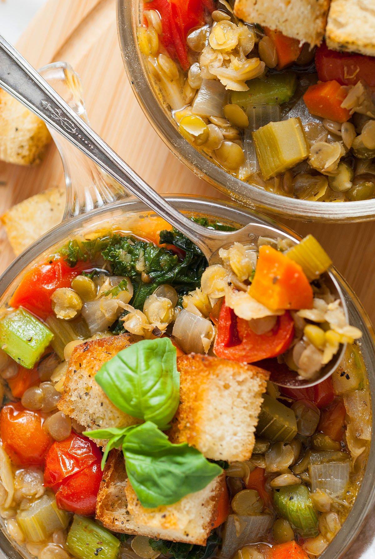Ιταλική Σούπα Φακής 4 Δύο μπολ Zuppa Di Lenticchie, μια χορταστική ιταλική σούπα λαχανικών με κρουτόν και φρέσκο βασιλικό, σερβιρισμένα με μεταλλικά κουτάλια.