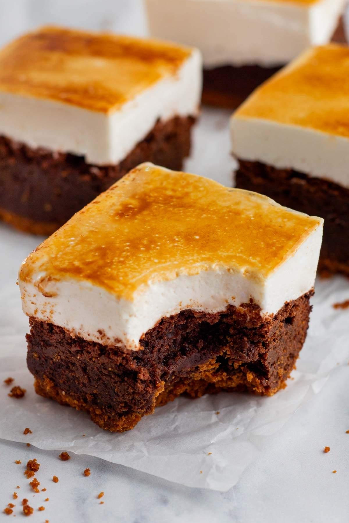 Κοντινό πλάνο ενός s'mores brownie που διαθέτει βάση μπράουνι, μια στρώση marshmallow και μια καραμελωμένη κορυφή. Από ένα κομμάτι έχει ληφθεί μια μπουκιά, αποκαλύπτοντας τις απολαυστικές στρώσεις και υφές.