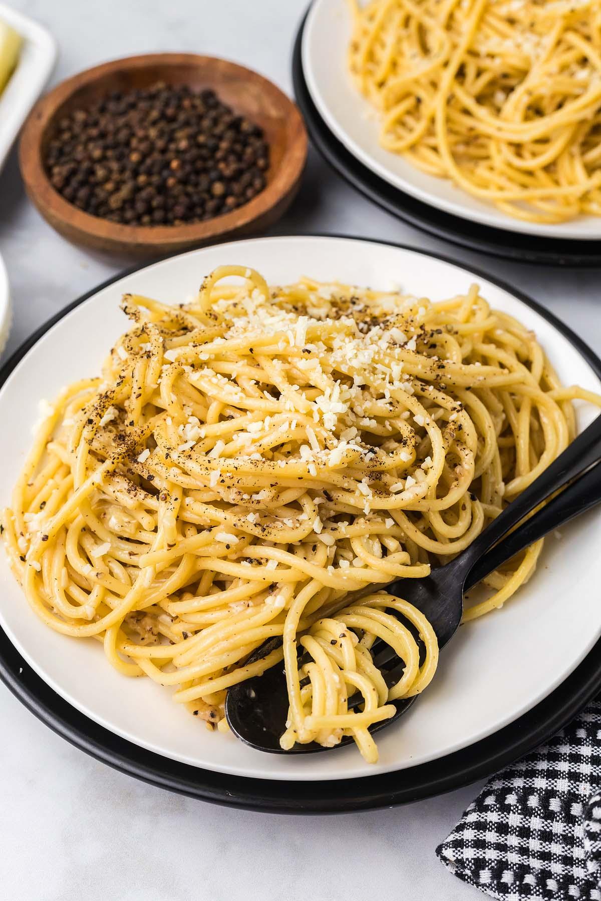 Τυρί και Πιπέρι 9 Ένα πιάτο cacio e pepe, με σπαγγέτι γαρνιρισμένα με τριμμένο τυρί και πιπέρι, κομψά σε συνδυασμό με ένα μαύρο πιρούνι. Επιπλέον πιάτα και μπολ γεμάτα πιπέρι βρίσκονται δελεαστικά στο βάθος.