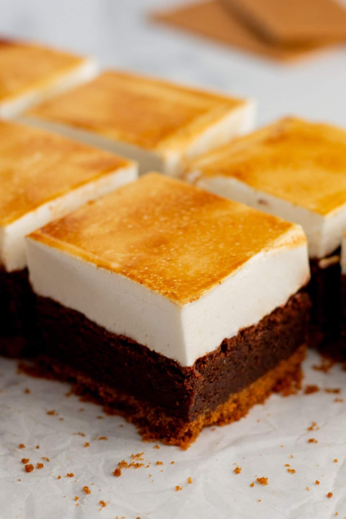 Κοντινό πλάνο κομμένων s'mores brownies με βάση μπισκότου graham cracker, σκούρα σοκολατένια μέση στρώση και καστανή επάνω στρώση ψημένης μαρσμελο-όμορφης επικάλυψης.