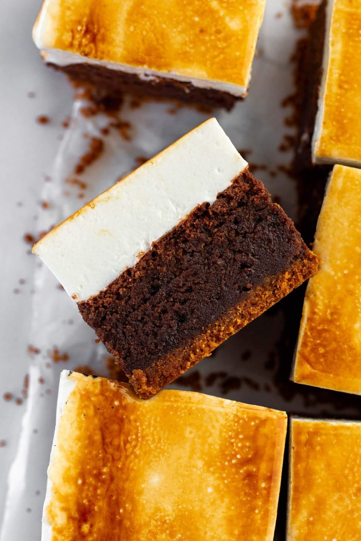 Ένας δίσκος με τετράγωνα s'mores brownies με σκούρα σοκολατένια βάση και ψητή λευκή επικάλυψη. Μια μπάρα είναι γωνιακή διαφορετικά από τις υπόλοιπες, τονίζοντας τις ξεχωριστές στρώσεις.