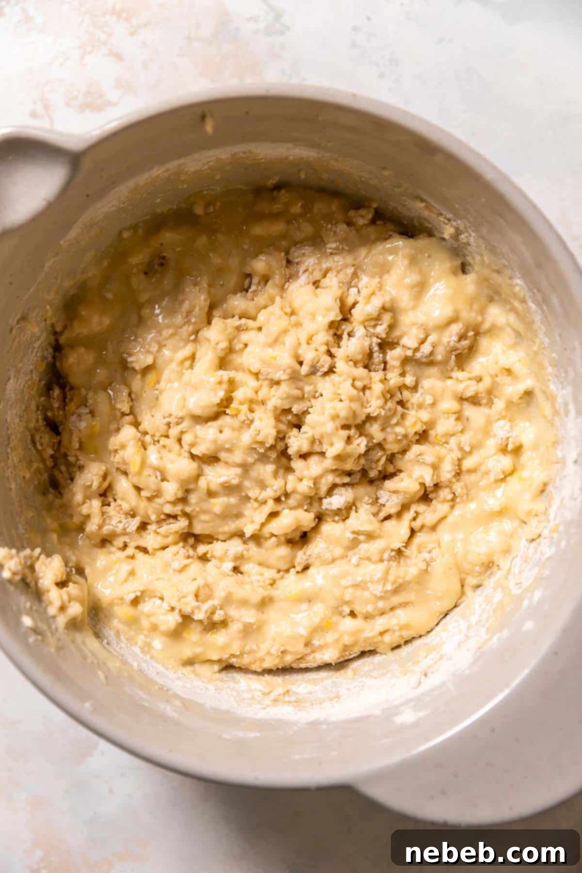 A mixing bowl with the lemon muffin batter before adding the raspberries, showing a lumpy but combined texture.