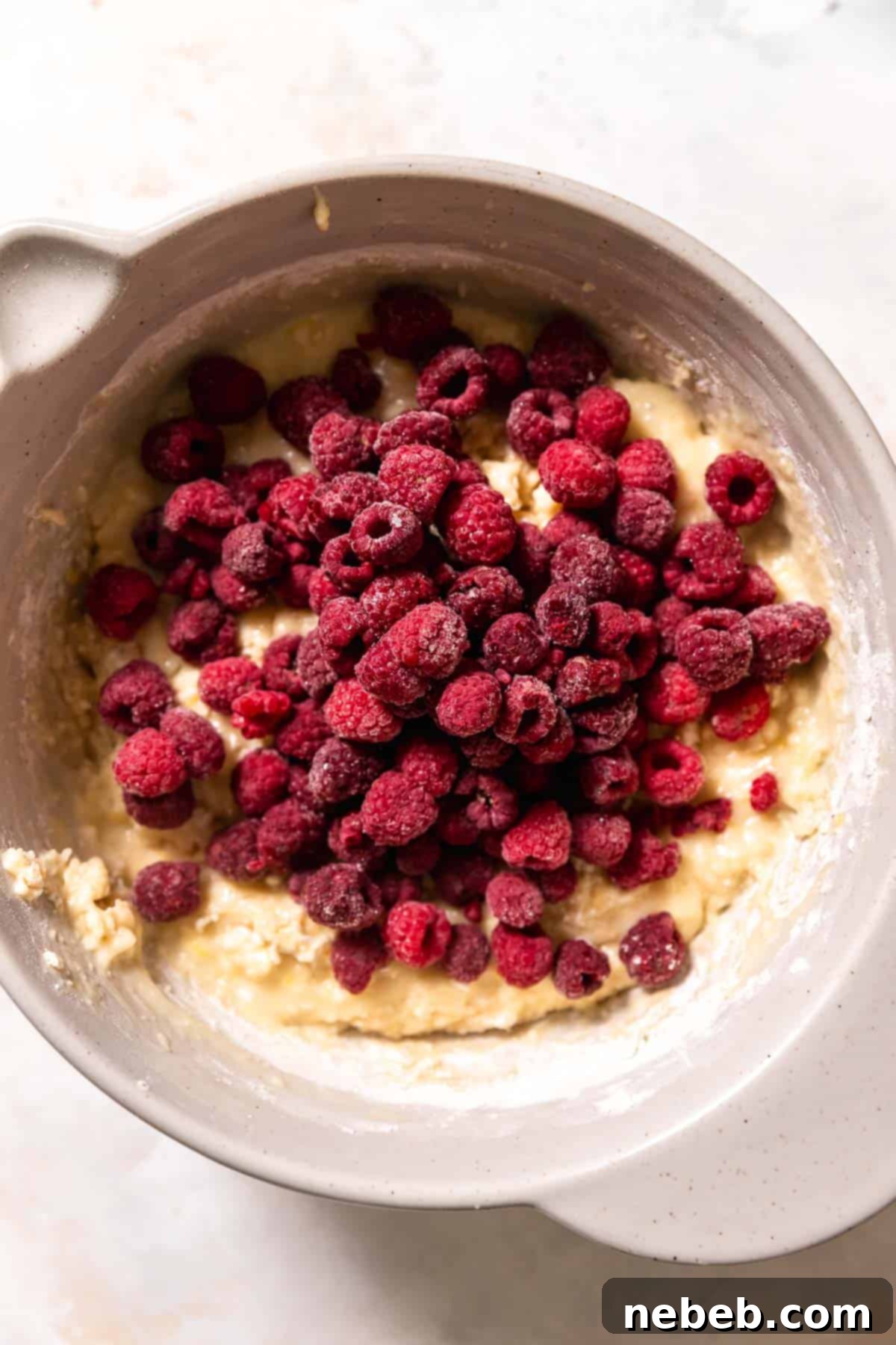 An overhead shot of the muffin batter in a bowl with frozen raspberries on top, ready for mixing.
