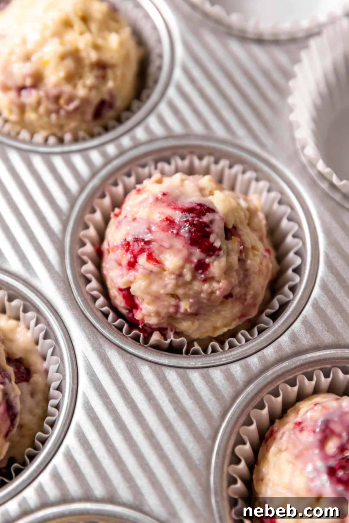 A muffin pan with lemon raspberry muffin batter scooped into the liners, filled generously.