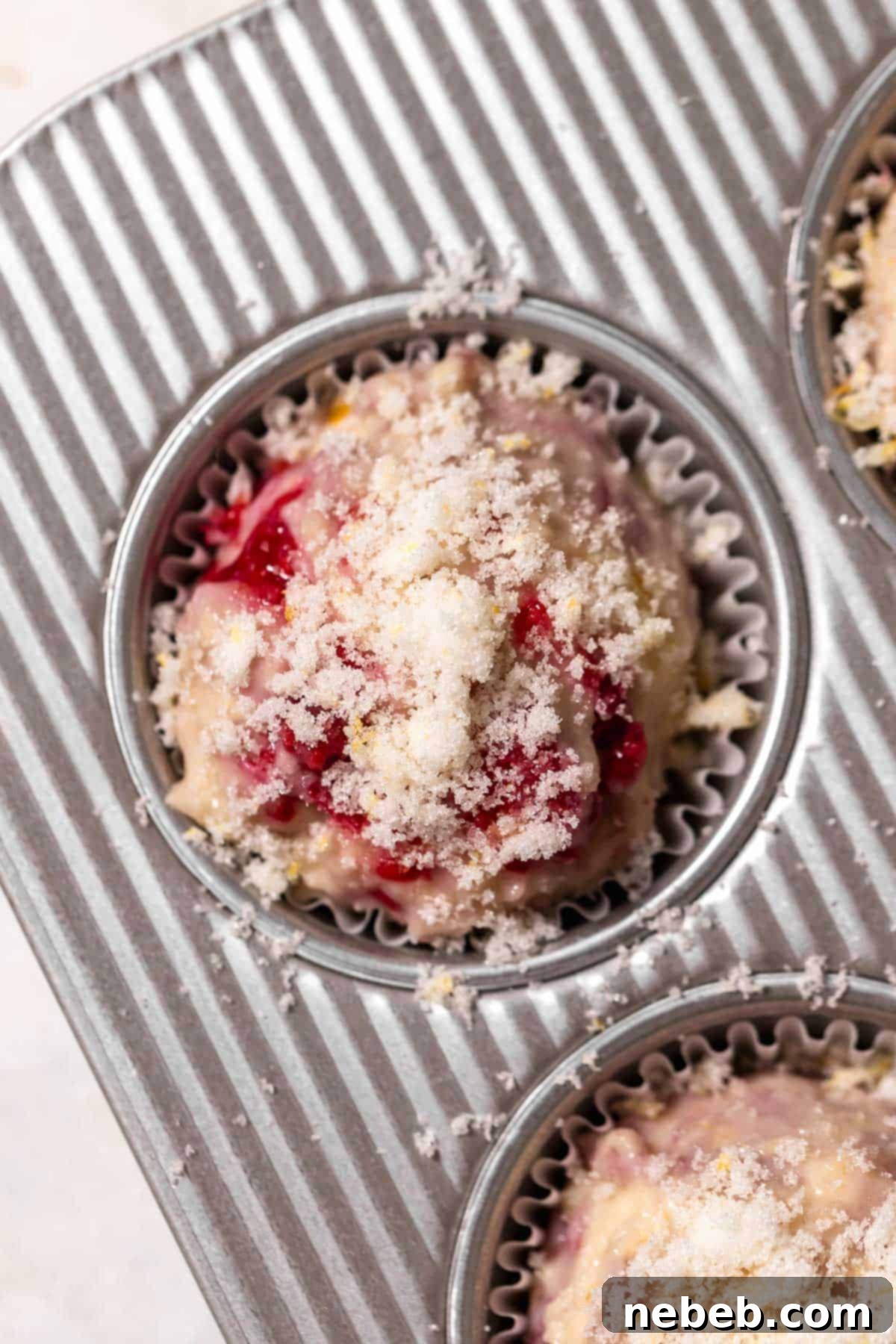 An overhead shot of the raspberry muffin batter topped with lemon sugar in a muffin pan, ready for baking.