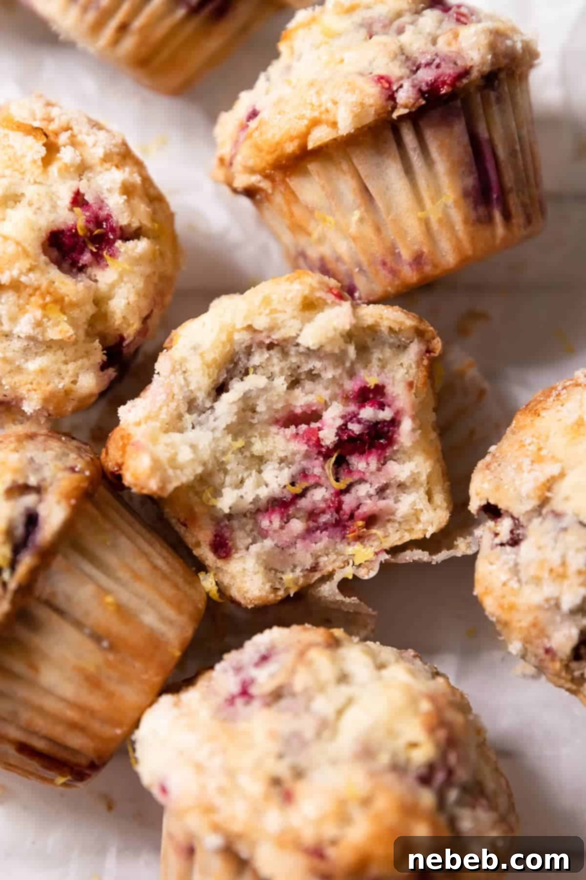 A perfectly moist lemon raspberry muffin on its side with a bite taken out of it, showing the juicy raspberries and fluffy texture, garnished with fresh lemon zest.