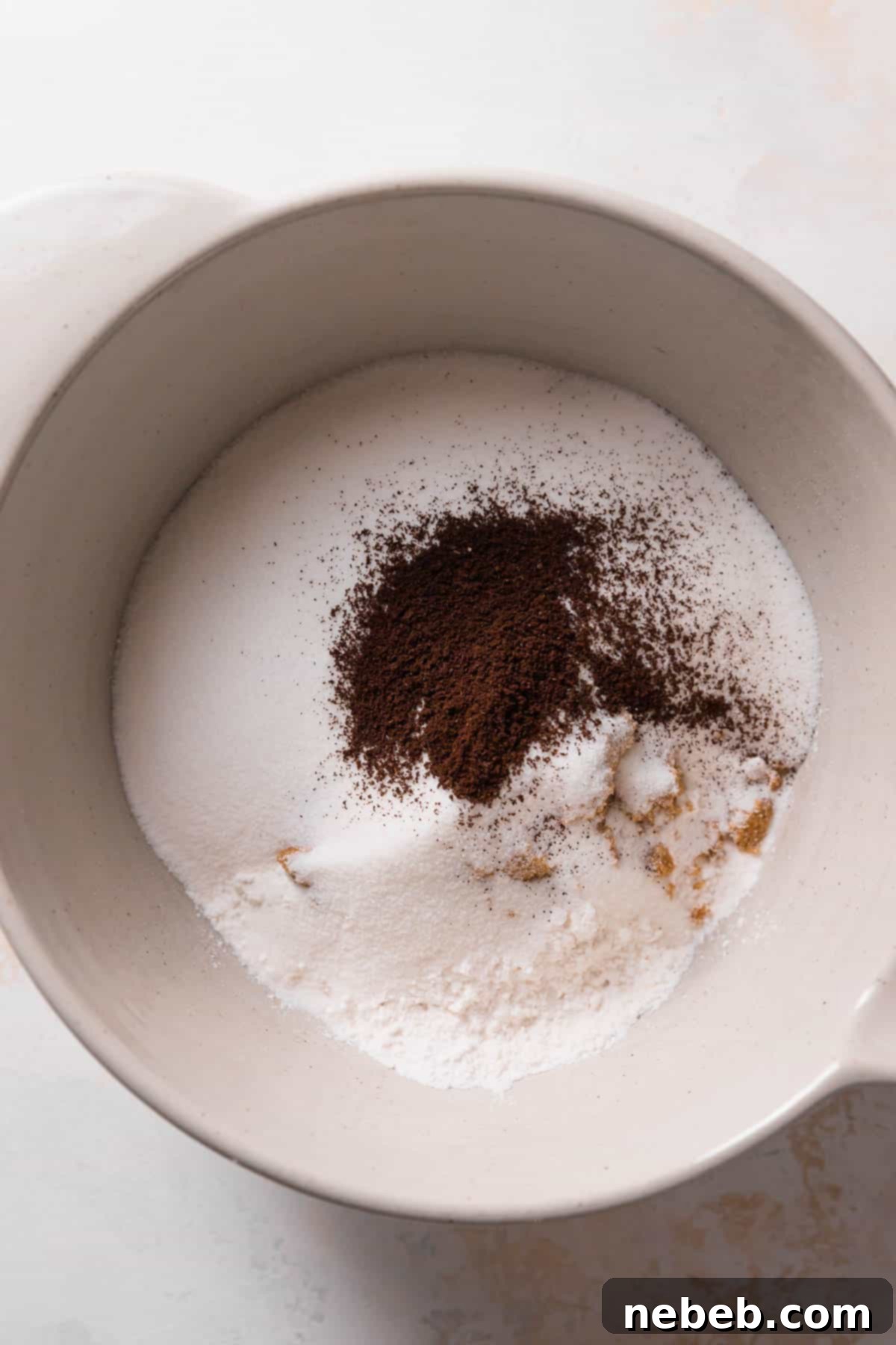 A mixing bowl holding dry ingredients like cake flour, granulated sugar, dark brown sugar, and cocoa powder, ready for the next step of mixing with butter.
