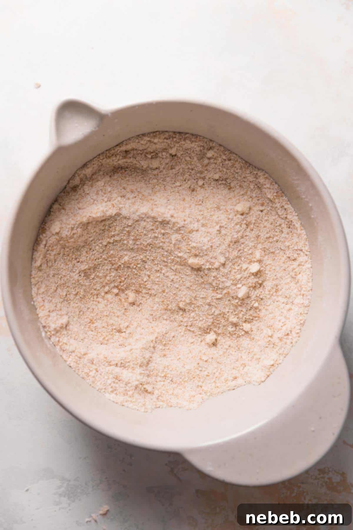 A mixing bowl showing dry ingredients blended with softened unsalted butter, creating a coarse, sandy texture as part of the reverse creaming method.