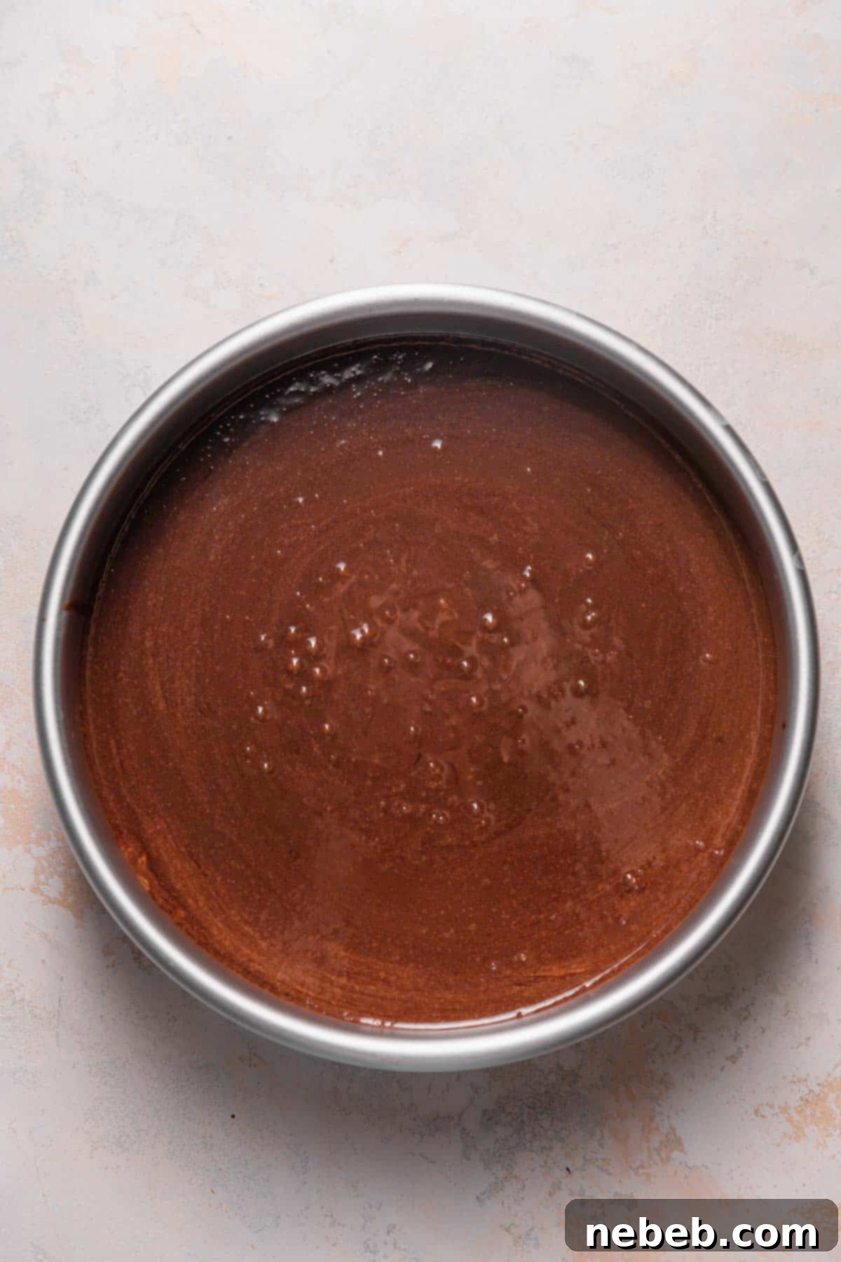 Dark, rich chocolate cake batter poured evenly into a prepared round cake pan, ready for its bake to transform into a delicious chocolate coffee cake layer.