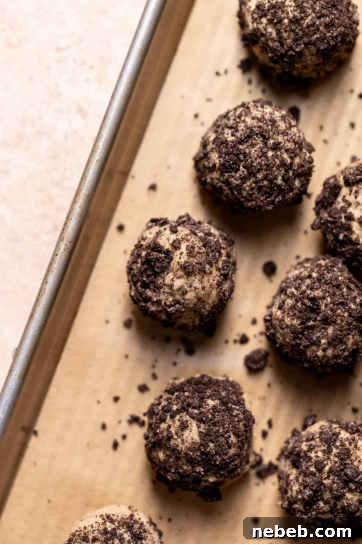 Cookie dough balls rolled in Oreo crumbs on a baking tray, ready for chilling.