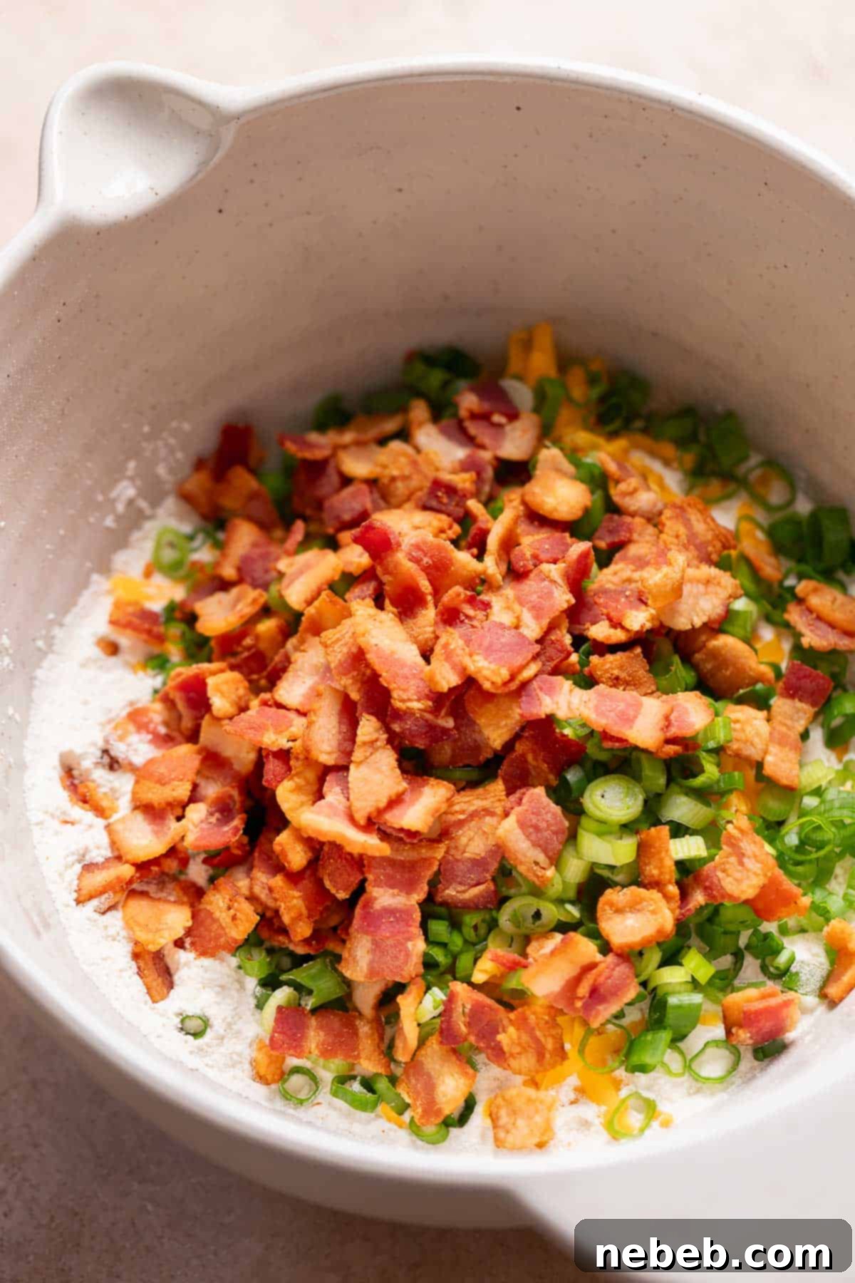 A mixing bowl with the dry ingredients, bacon, cheese, and scallions before mixing.