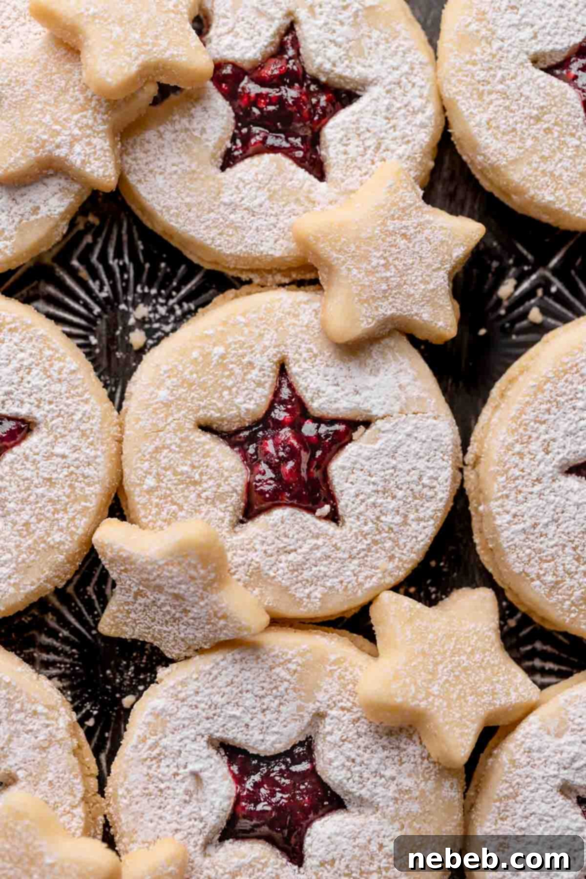 Close-up of a festive Linzer tart cookie with a bright raspberry jam filling, presented on a black baking tray, ready for holiday celebrations.