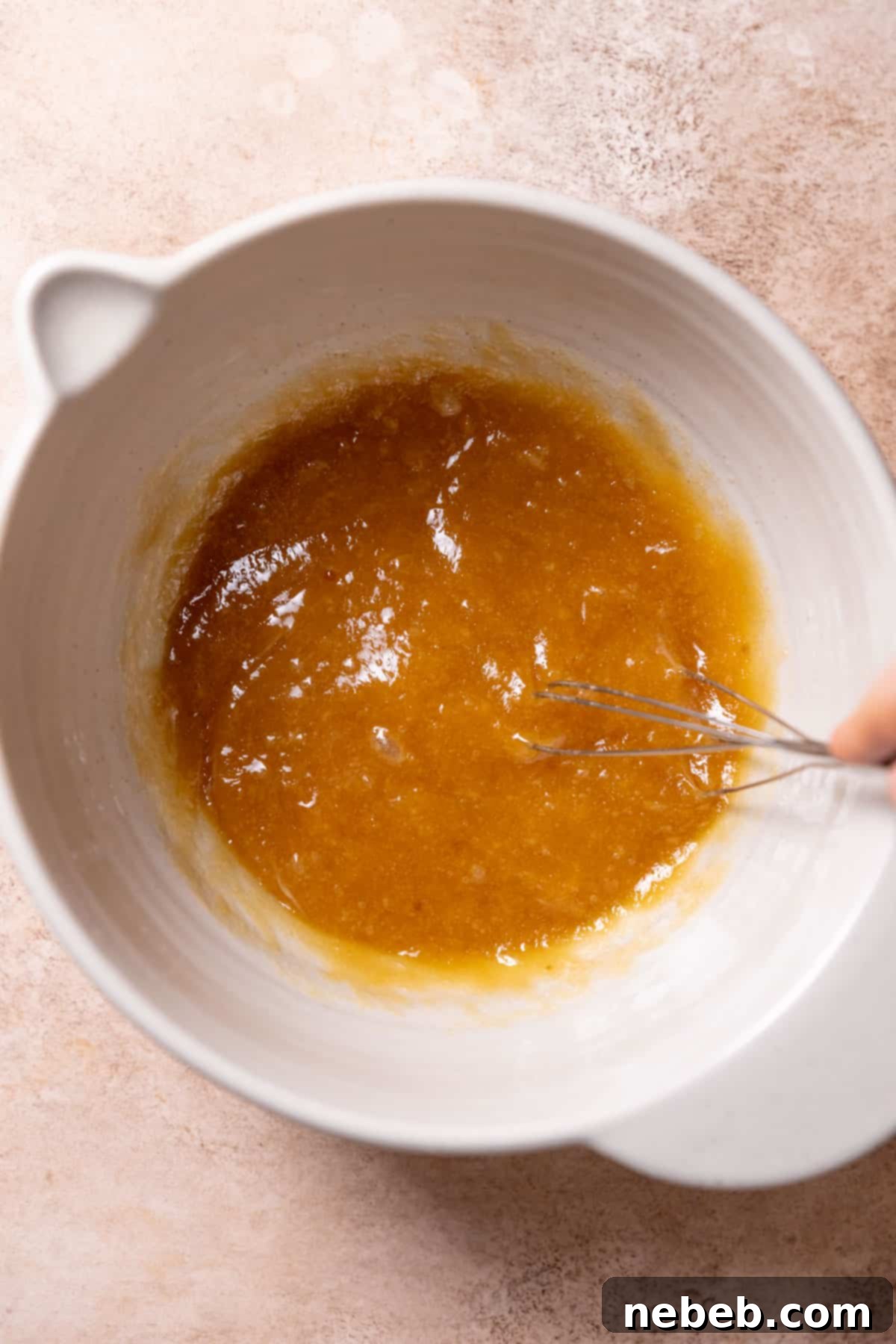 A mixing bowl with melted butter, granulated sugar, brown sugar, eggs, and vanilla extract whisked together, appearing glossy and slightly thickened.