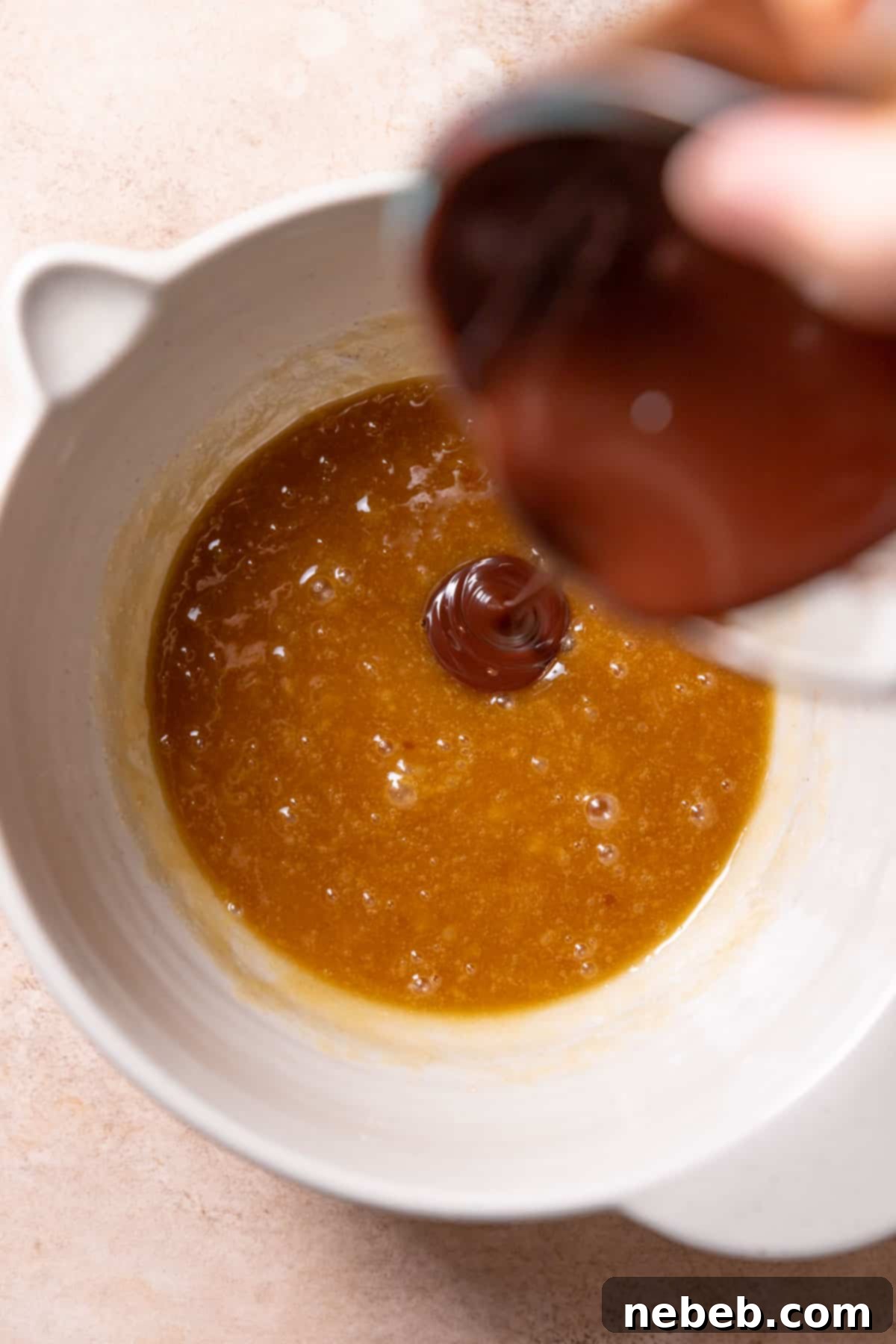 Melted dark chocolate being poured into the whisked wet ingredients in a mixing bowl.