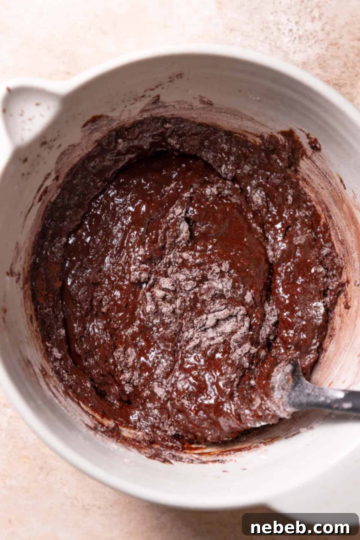 Dry flour, cocoa powder, baking powder, and salt being gently folded into thick brownie cookie batter with a rubber spatula.