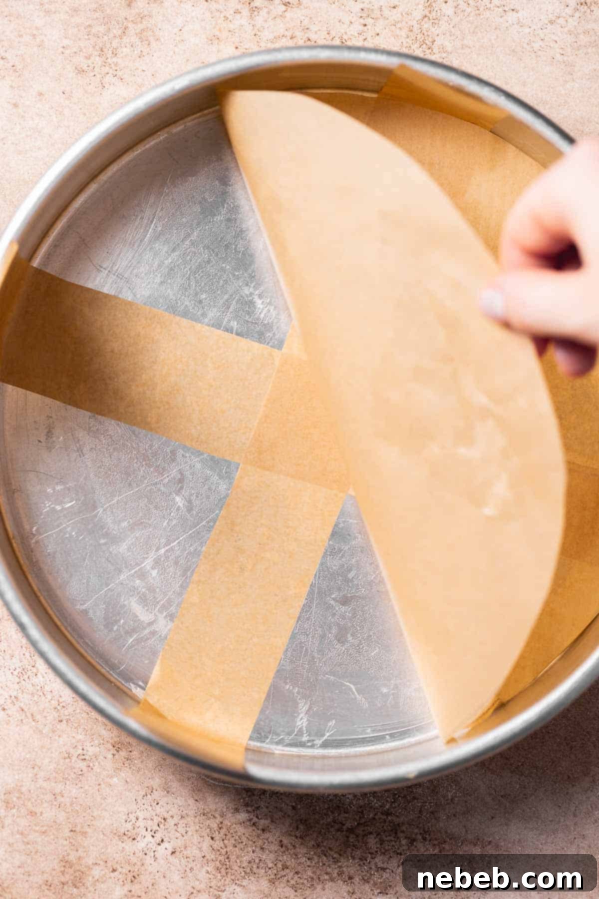 A round cake pan being lined with parchment paper.