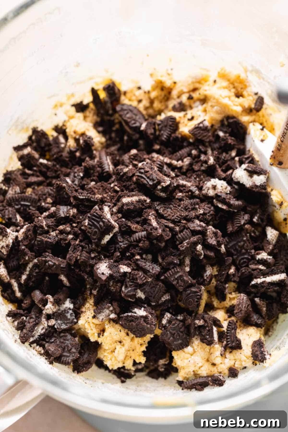 A mixing bowl with chopped oreo cookies on top of the cookie dough before mixing.
