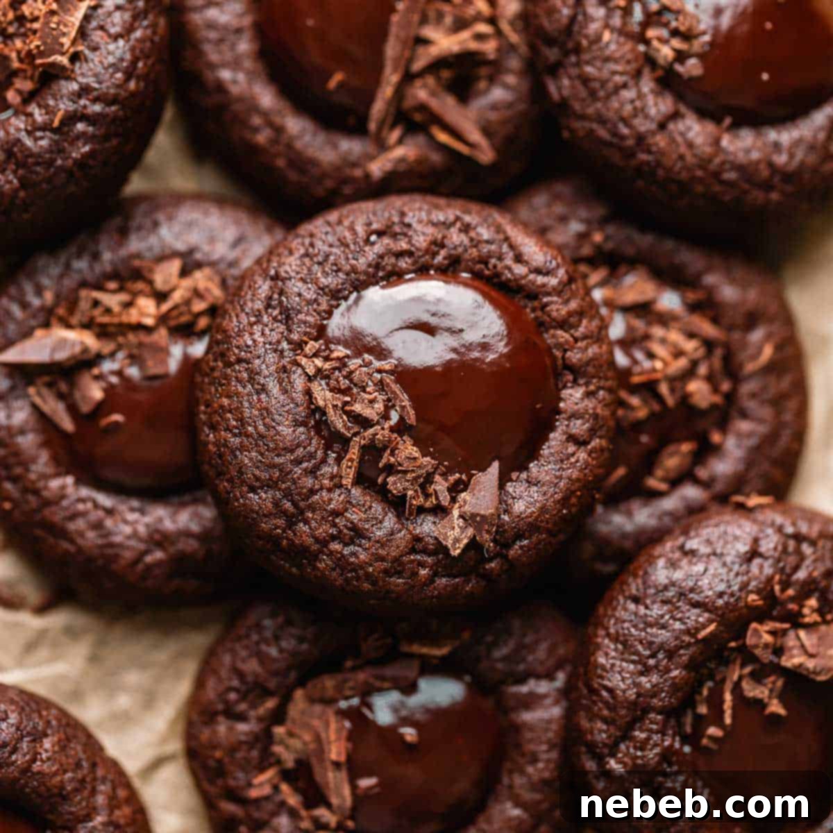 Close-up of chocolate thumbprint cookies filled with glossy chocolate ganache and garnished with chopped chocolate.