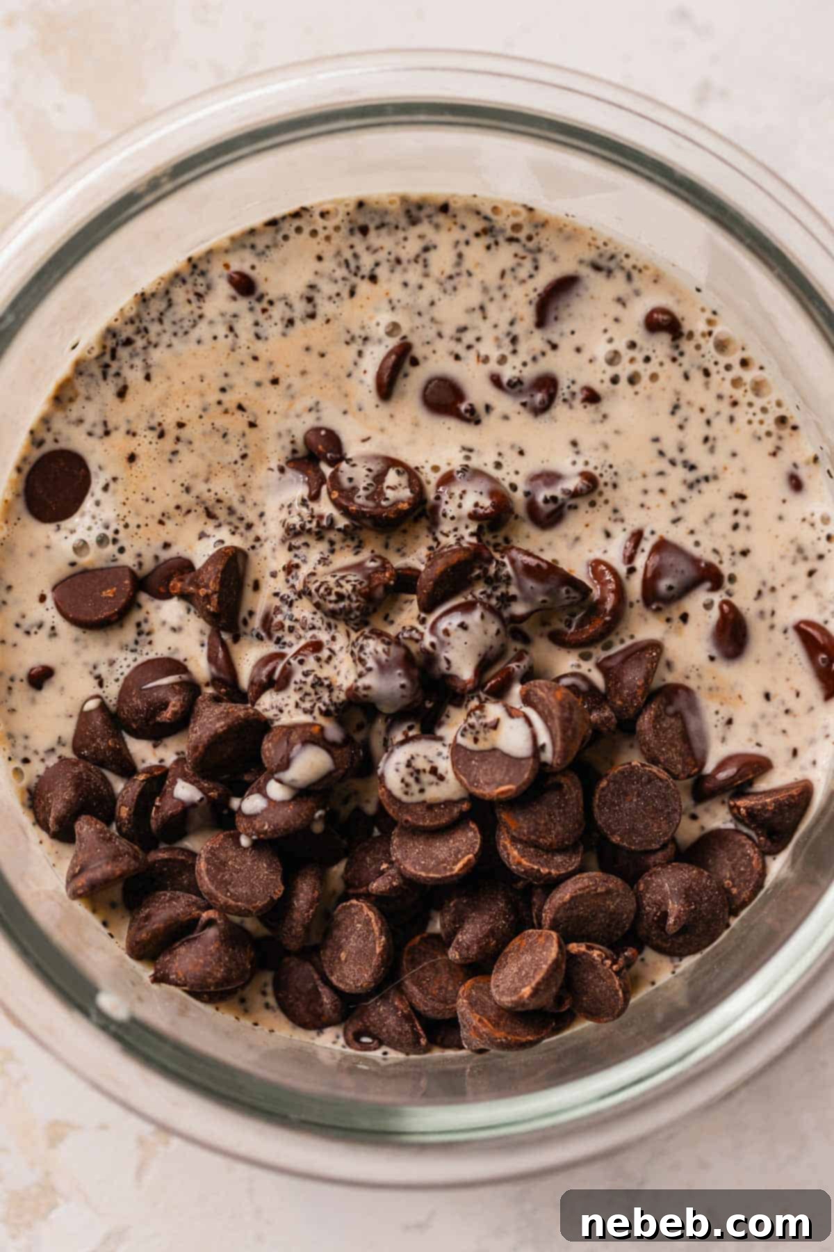 Semisweet chocolate chips and ground espresso in a glass bowl, with hot heavy cream being poured over them.