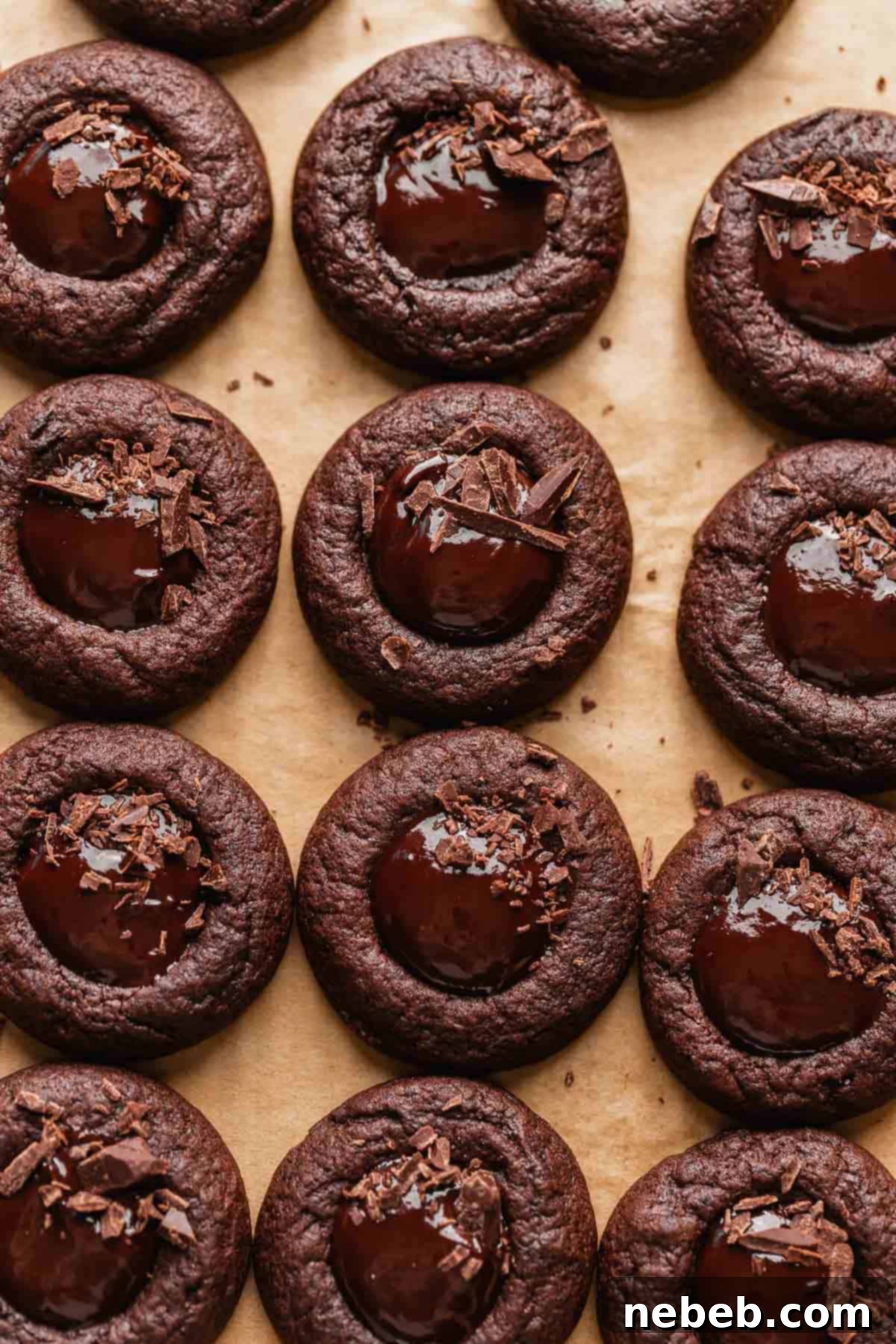 Baked chocolate thumbprint cookies with ganache filling, garnished with chopped chocolate, on a baking tray.