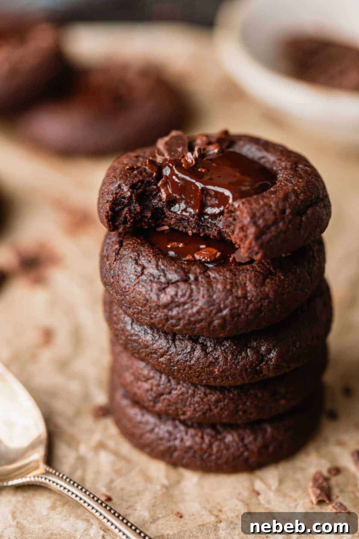 A stack of three chocolate thumbprint cookies, with the top one having a bite taken out to reveal the gooey ganache center.
