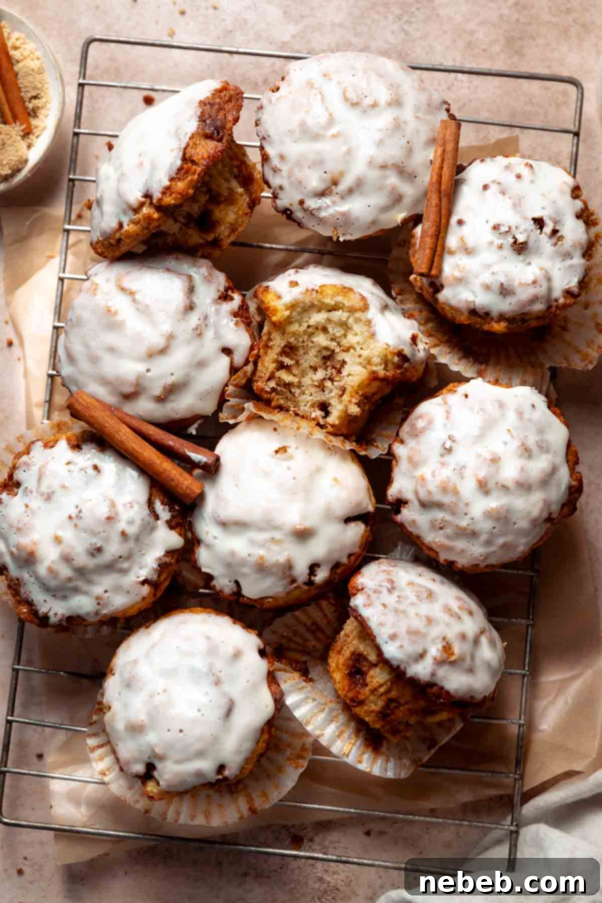 Cinnamon bun muffins covered in cream cheese icing on a wire cooling rack.