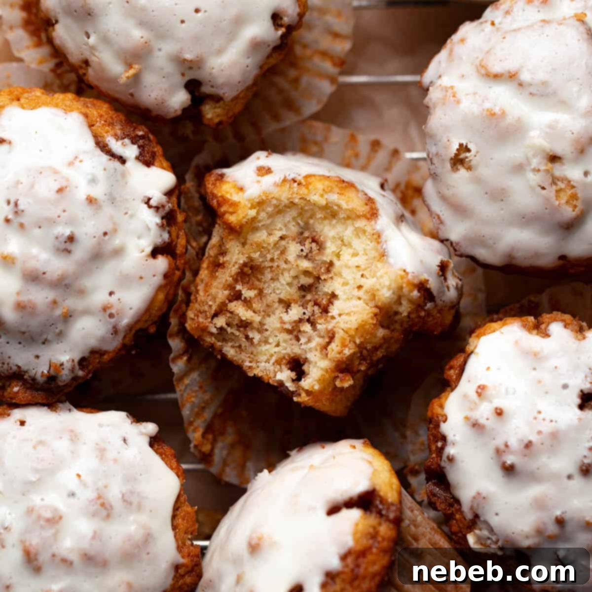 Cinnamon roll muffin with a bite taken out of it on a wire cooling rack.