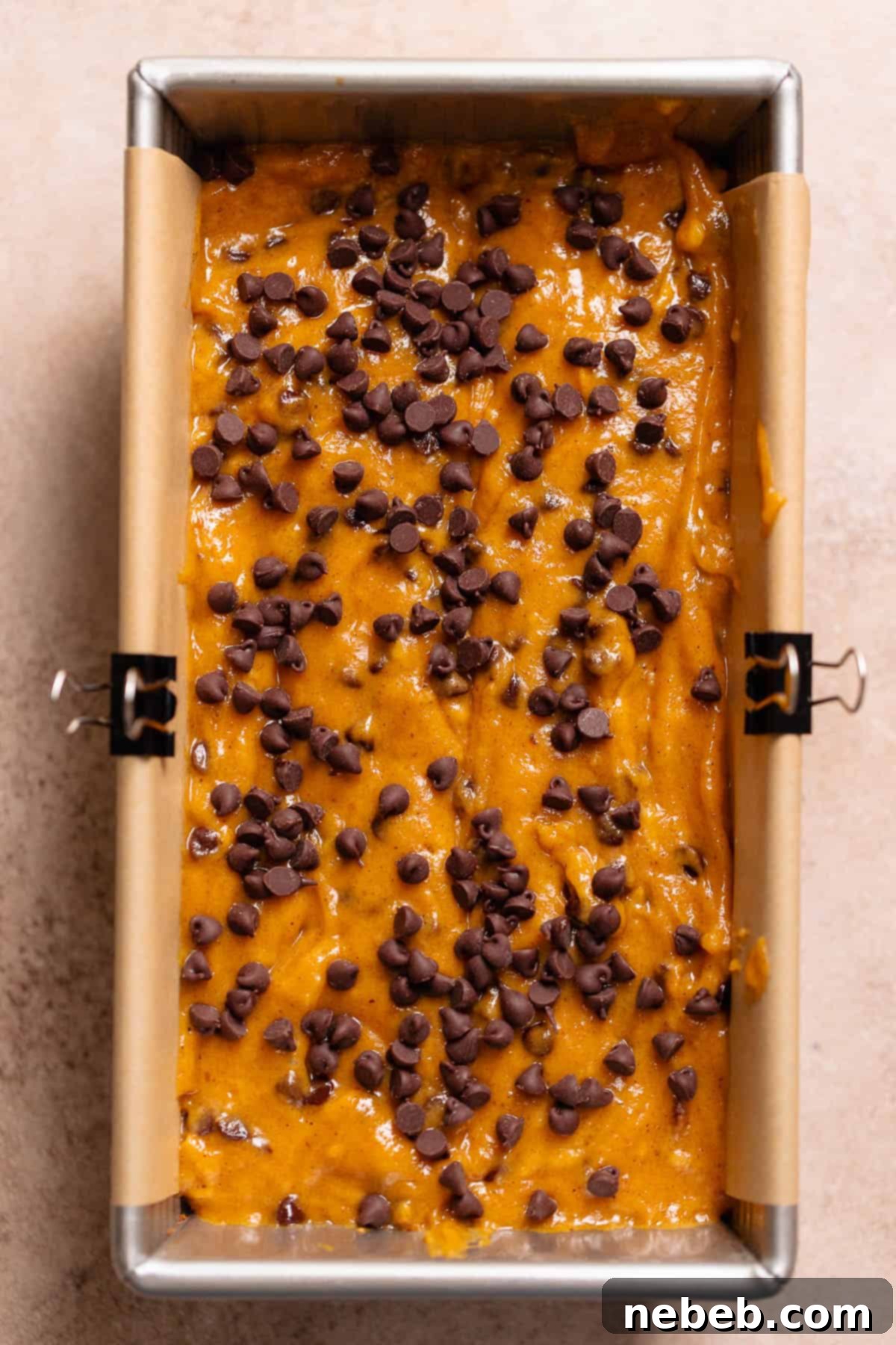 Rich chocolate chip pumpkin bread batter poured into a parchment-lined loaf pan, ready for baking.