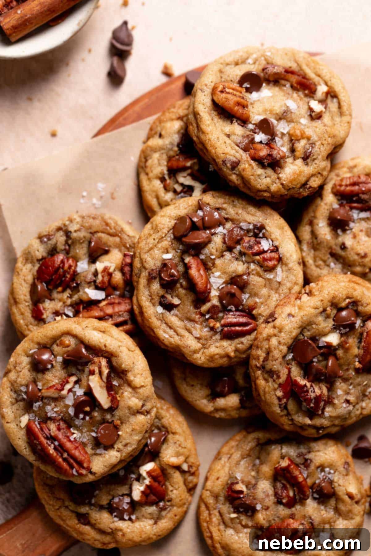 A pile of golden-brown chocolate chip pecan cookies, generously topped with flaky sea salt and glistening melted chocolate chips, beckoning a bite.