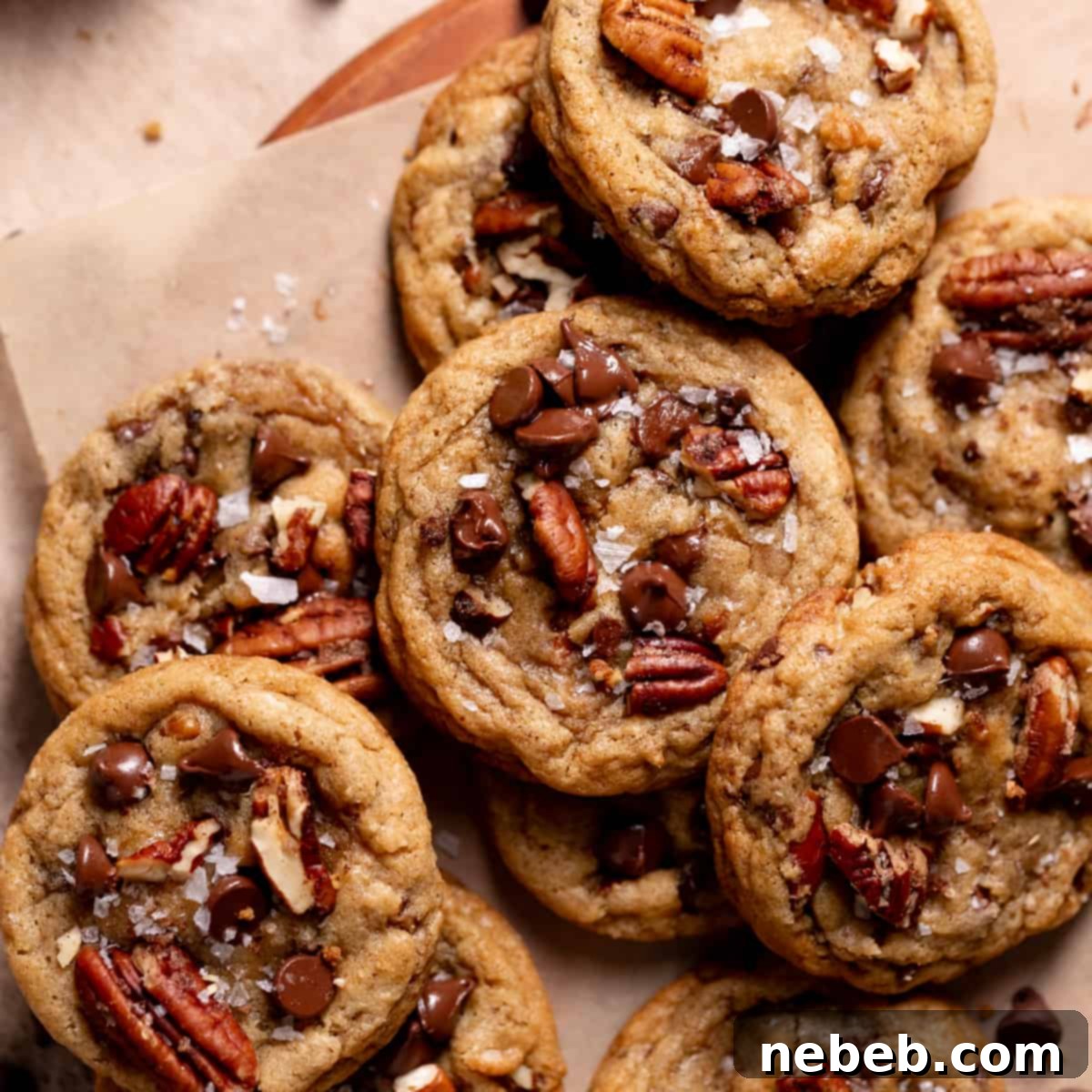 A tantalizing pile of warm chocolate chip pecan cookies, generously topped with an extra sprinkle of chocolate chips and flaky sea salt, inviting you to take a bite.