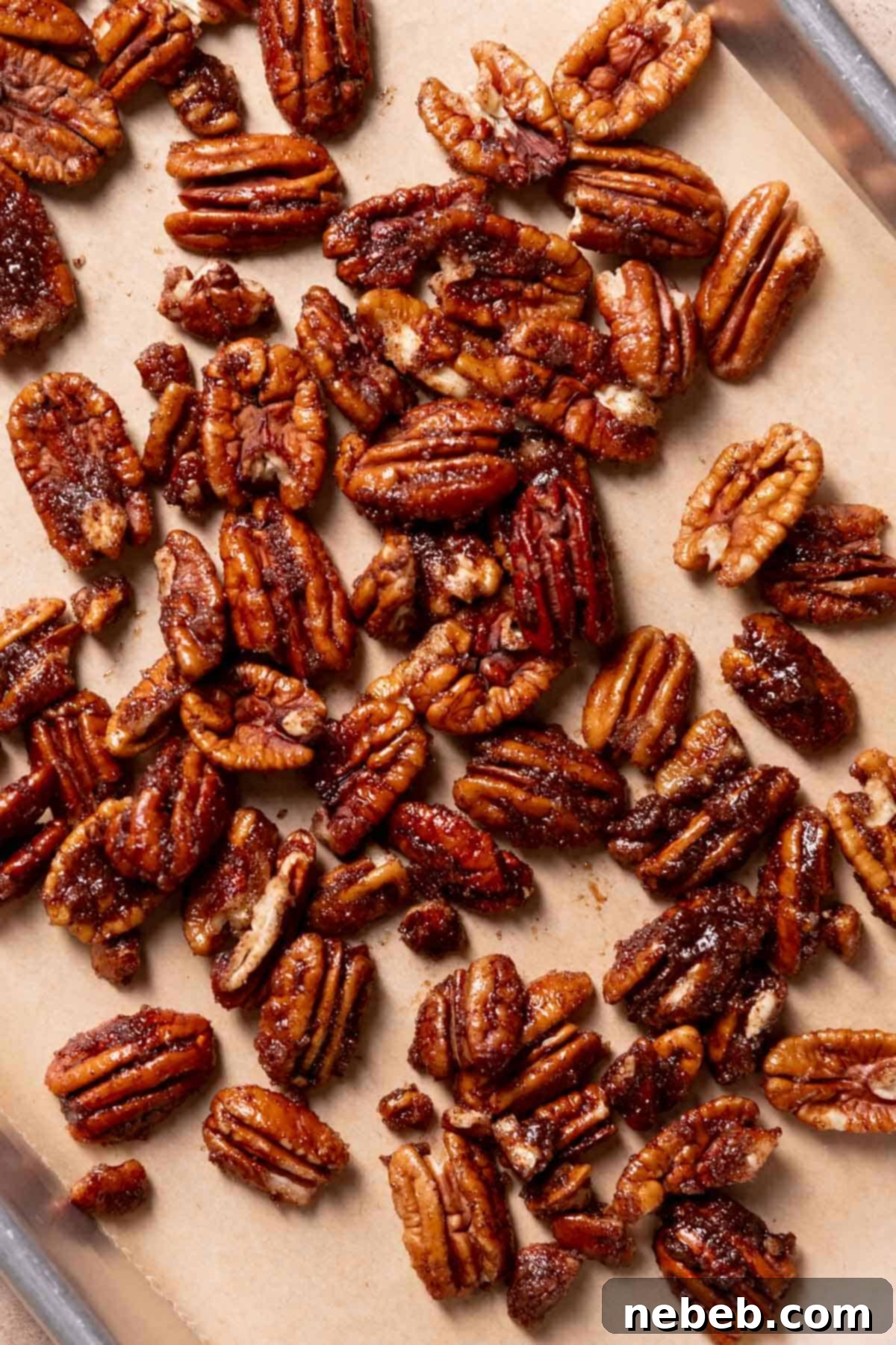 Pecan halves evenly coated in melted butter, granulated sugar, and cinnamon, spread on a baking tray lined with parchment paper, ready for roasting.