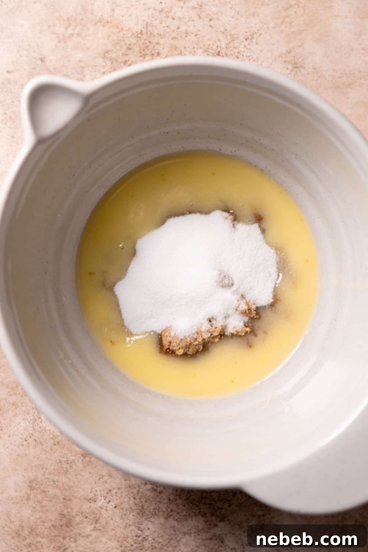A large mixing bowl containing melted butter, light brown sugar, and granulated sugar, ready to be whisked together.