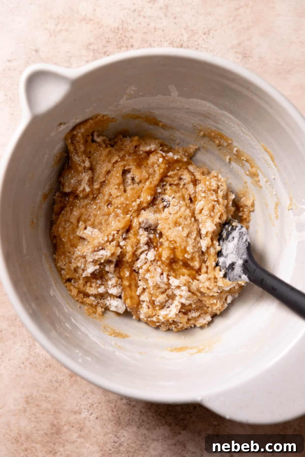 Dry ingredients, including flour, baking soda, and salt, being gently folded into the wet cookie dough mixture with a rubber spatula in a mixing bowl.