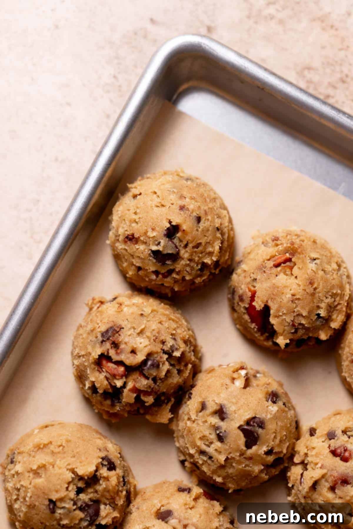 Scooped chocolate pecan cookie dough balls arranged on a parchment-lined baking tray, ready for freezing and baking.